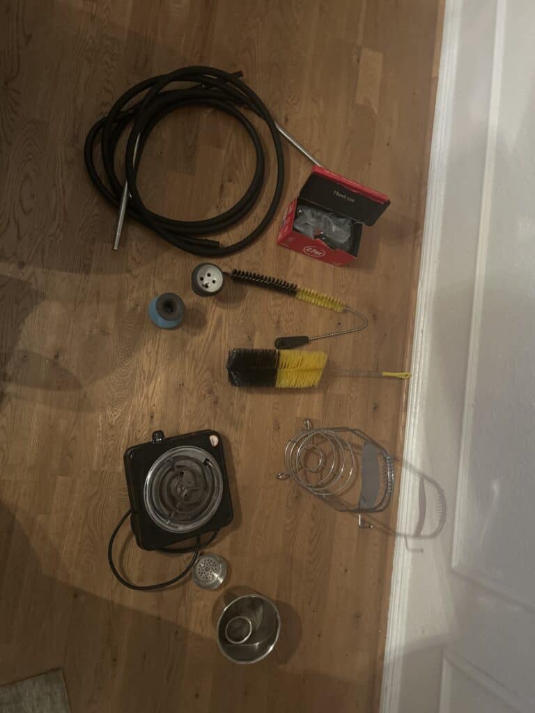 Verschiedene Shisha-Teile und Zubehör auf Holzboden.