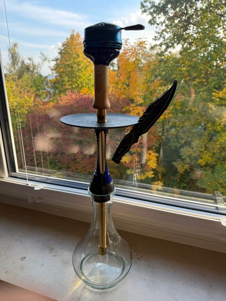 Shisha mit Glasbowl, Kohleanzünder und Zange auf Fensterbank.