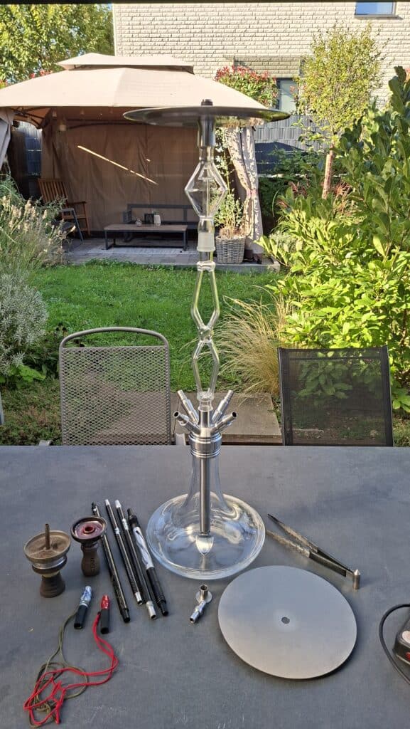Großer Shisha-Kopf mit Glasbowl, Schlauch und Zubehör auf Tisch.